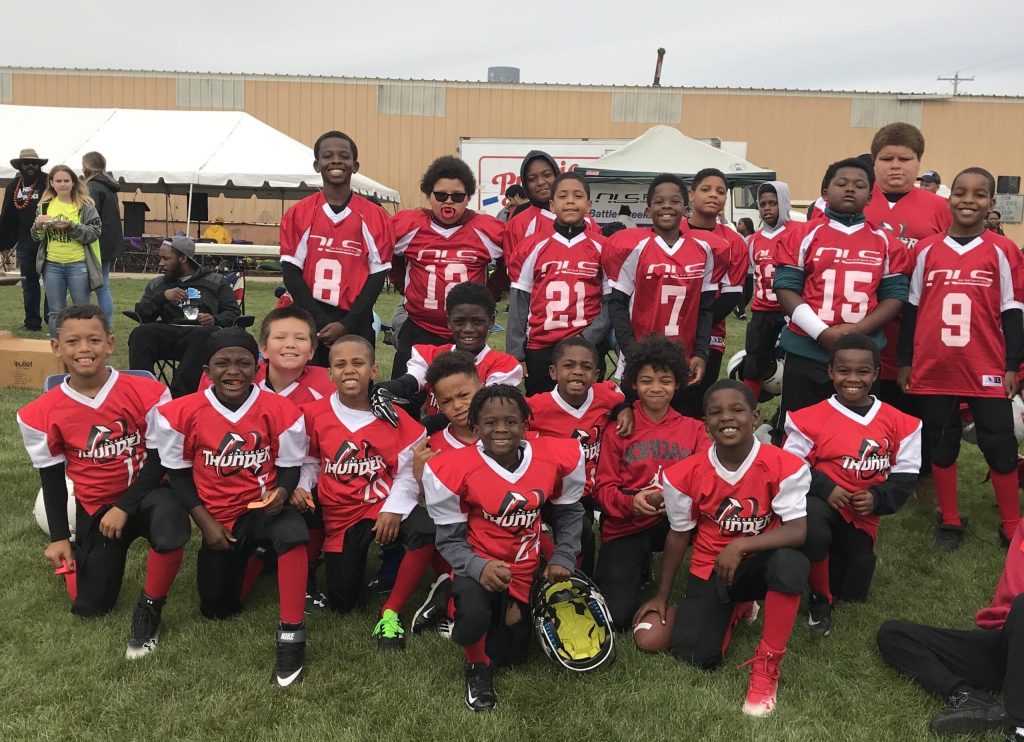 A youth football team in red jerseys poses together on a grassy field, smiling for a group photo.