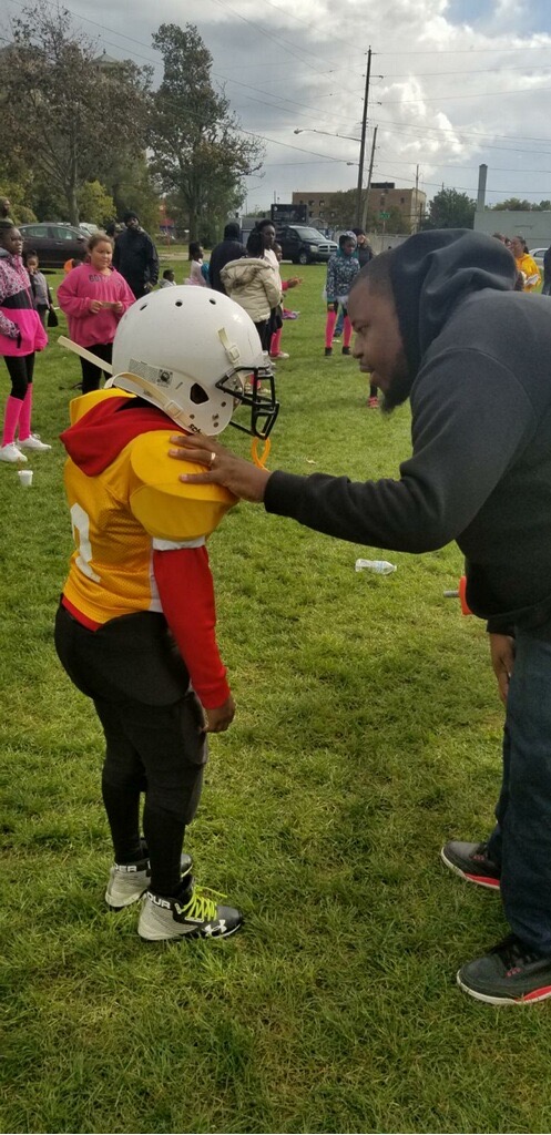 A coach encourages a young football player on a grassy field during a game.