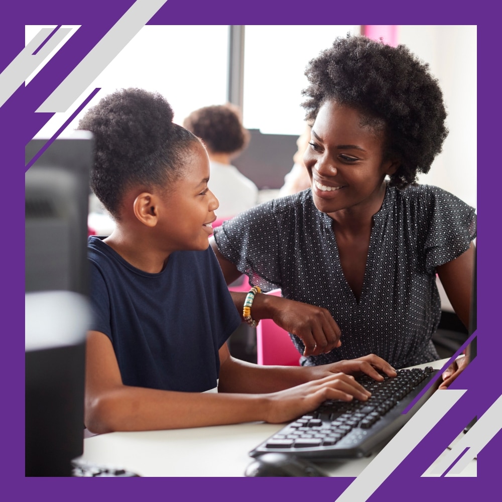 A woman smiles at a girl using a computer in a classroom with a purple geometric border.