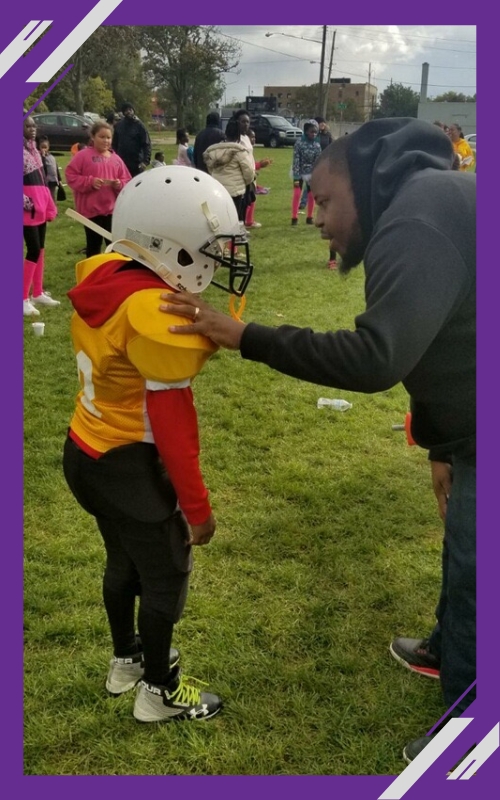 A coach encourages a young football player in yellow gear on a grassy field during a game.