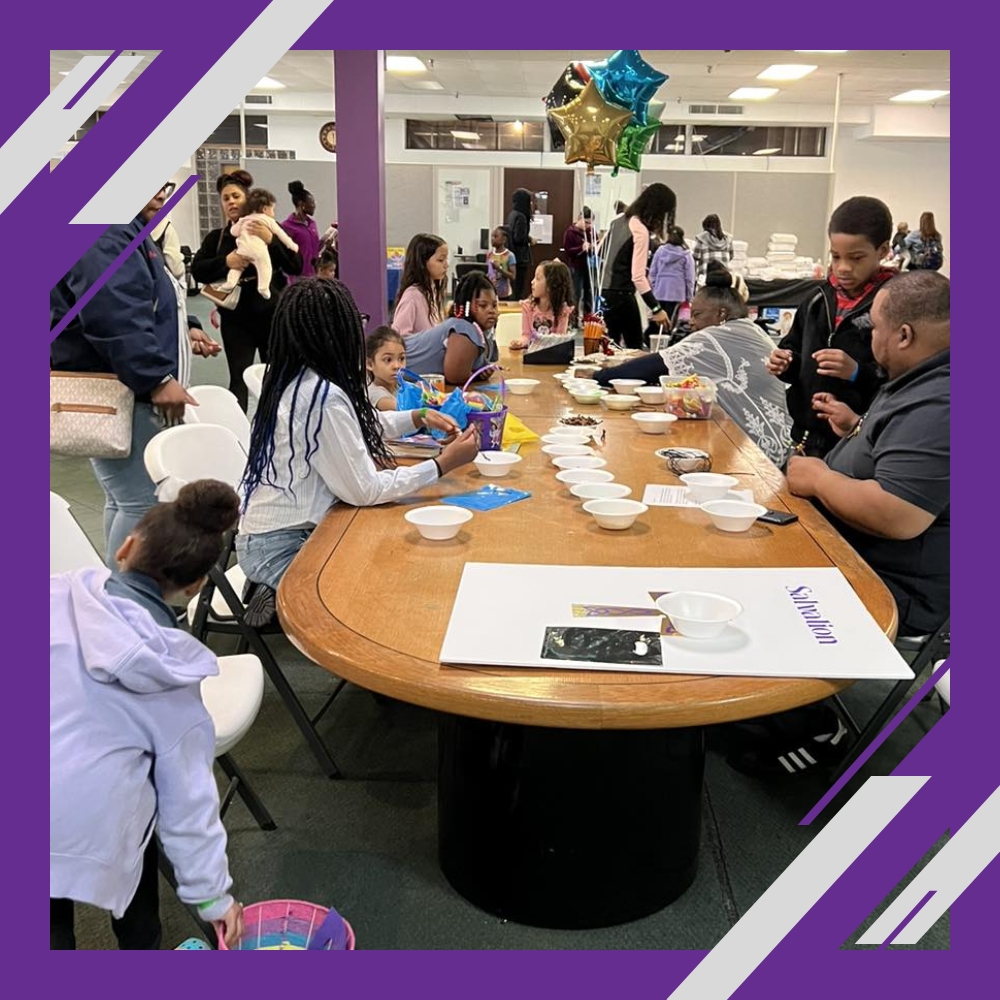Children and adults gather around a table with crafts and snacks at a lively indoor event.